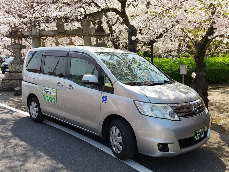 桜の木の下に停車する福祉タクシーにこにこのセレナ